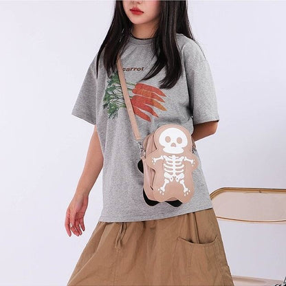 Person wearing a gray t-shirt with a graphic design and holding a pink skeleton bag.