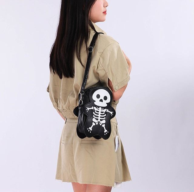 Person wearing a beige jacket with a black skeleton design bag on a white background