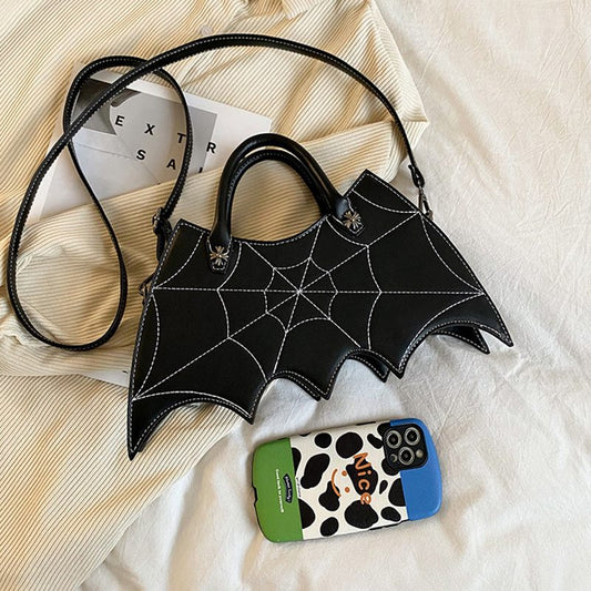 Black bat-winged handbag with a spider web design on a textured surface.