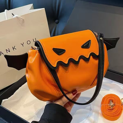 Orange pumpkin-shaped handbag with black accents held by a person, with a 'Thank You' bag in the background.