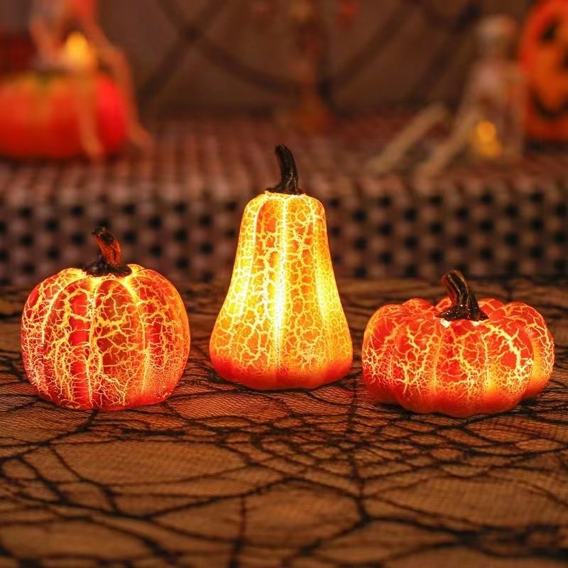 Three illuminated decorative pumpkins with a cracked texture on a textured surface.
