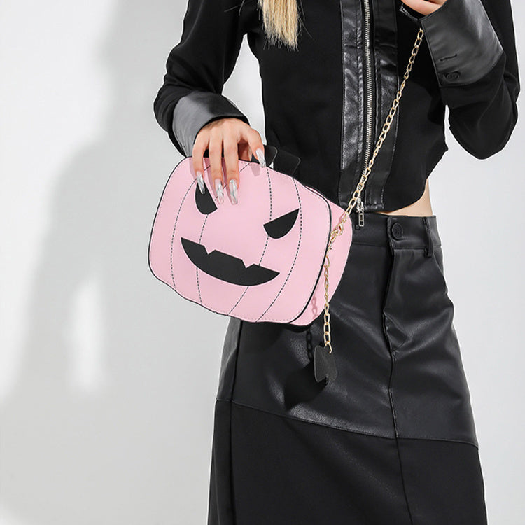 Person holding a pink pumpkin-shaped bag with a gold chain on a plain background