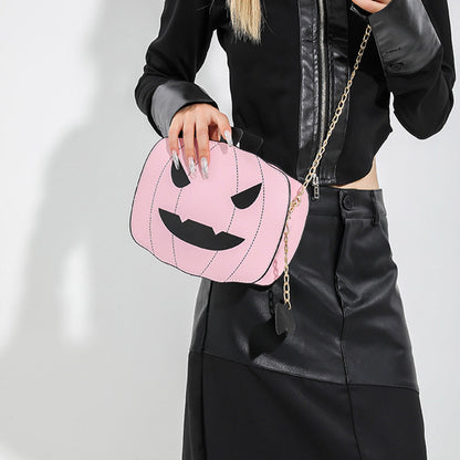 Person holding a pink pumpkin-shaped bag with a gold chain on a plain background