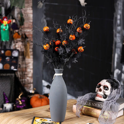 Halloween-themed decoration with black branches with small pumpkins, a gray vase, and a skull on books.