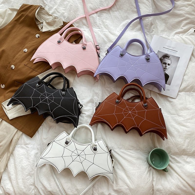 Set of bat-shaped handbags in various colors on a bed.