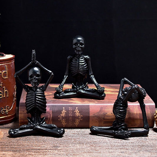 Three black skeleton figurines in various poses on a wooden surface with a dark background.