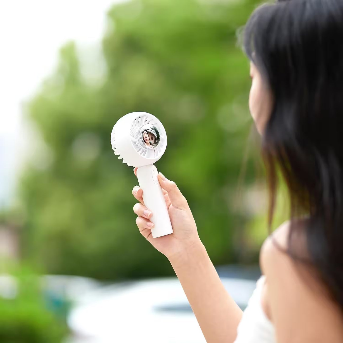 Person holding a white handheld device with a blurred green outdoor background