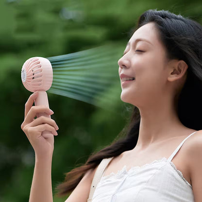 Woman using a pink handheld fan with a green blurred background