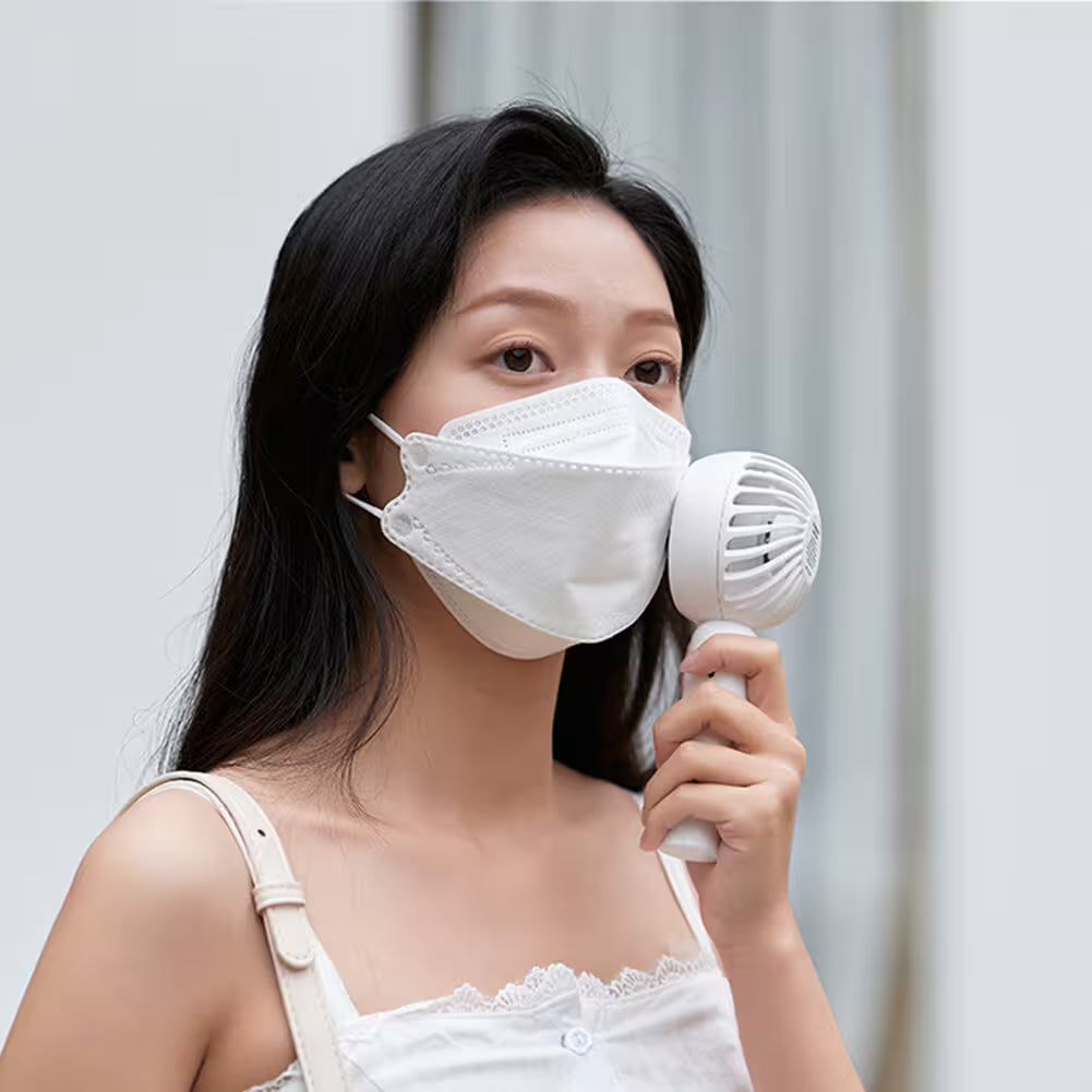 Woman wearing a white face mask holding a white hair dryer against a light gray background