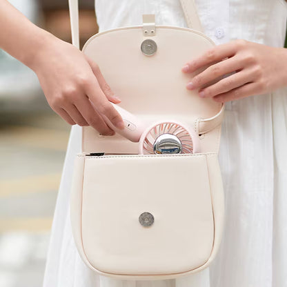 Person opening a beige handbag to reveal a pink handheld device with a fan-like design.