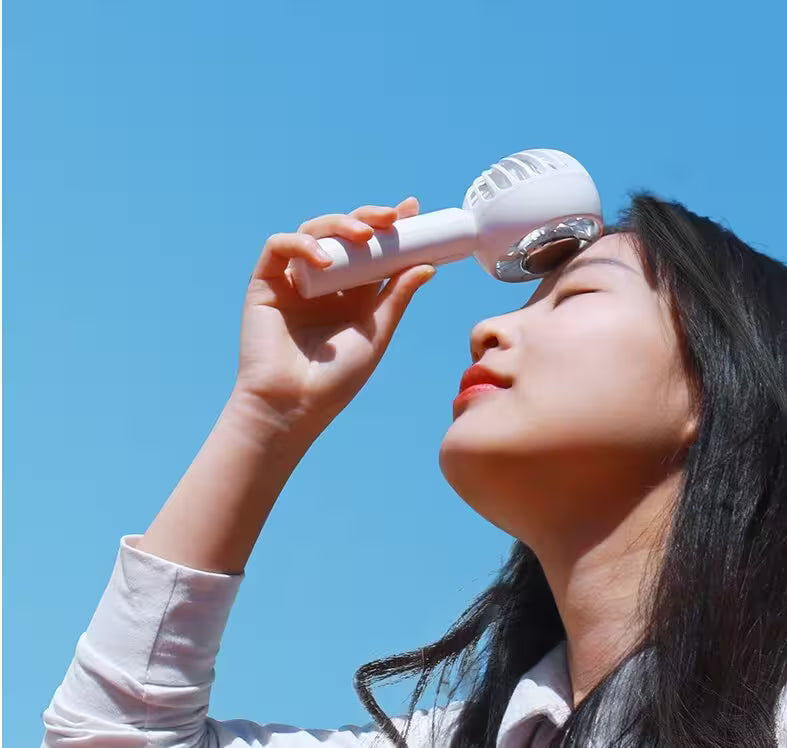 Person using a white facial cleansing brush against a clear blue sky