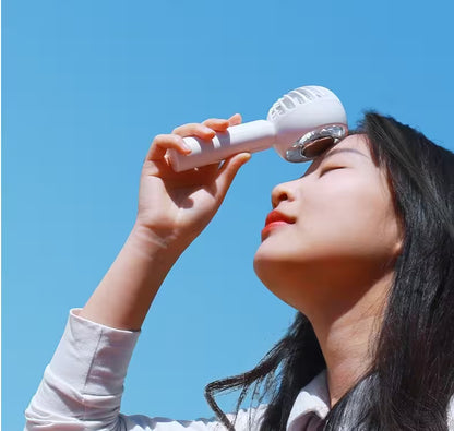 Person using a white facial cleansing brush against a clear blue sky