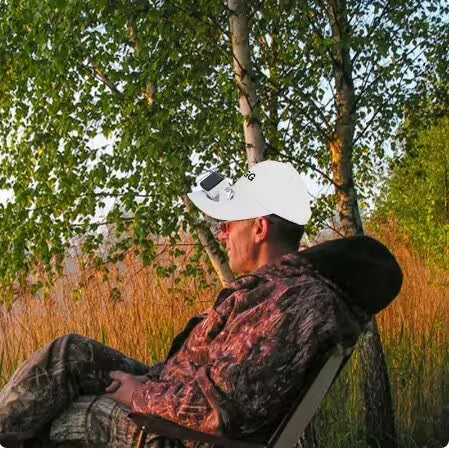 Man in camouflage clothing sitting in a chair among trees and grass
