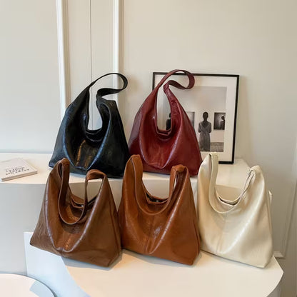 Five leather handbags in black, red, brown, and beige on a white surface with a framed picture in the background.