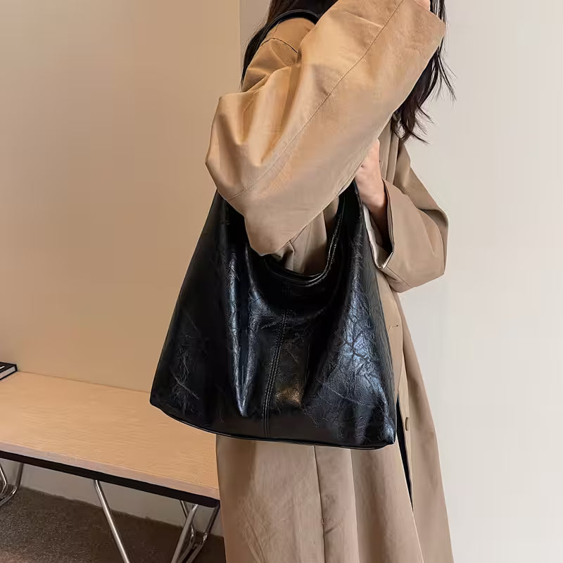 Person wearing a beige coat holding a black leather handbag indoors.