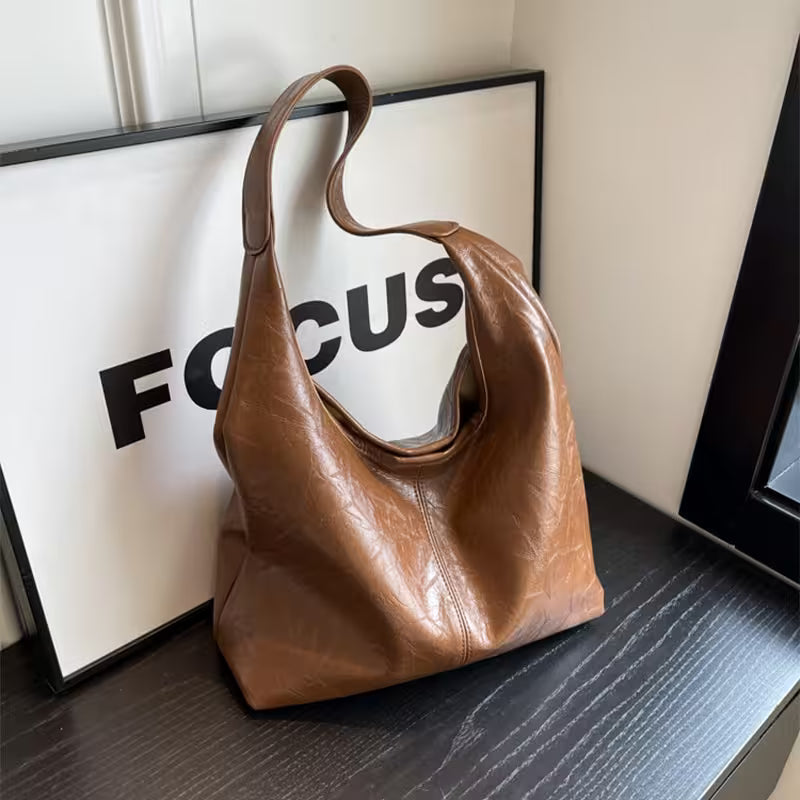 Brown leather handbag on a surface with a 'FOCUS' poster in the background