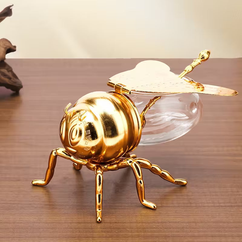 Gold bee-shaped object with a clear glass body on a wooden surface