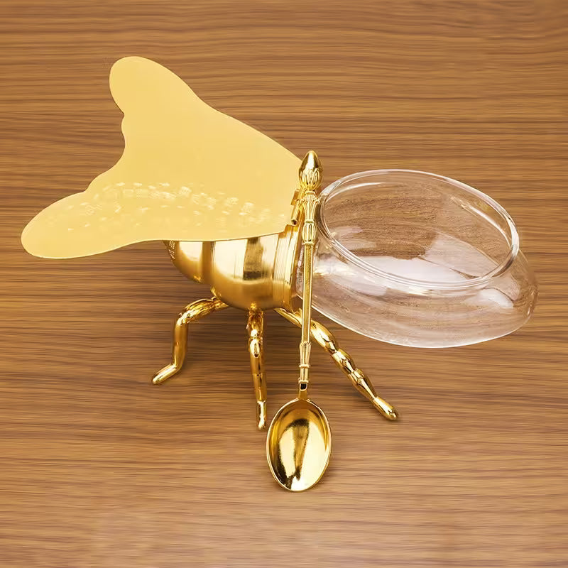 Gold bee-shaped container with a lid and spoon on a wooden surface