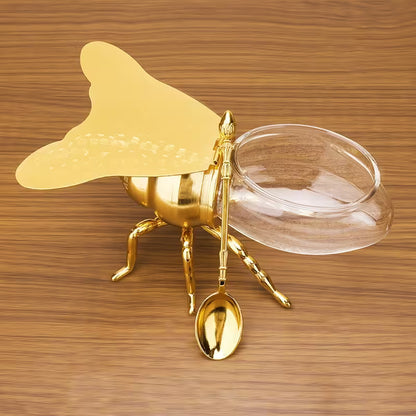 Gold bee-shaped container with a lid and spoon on a wooden surface