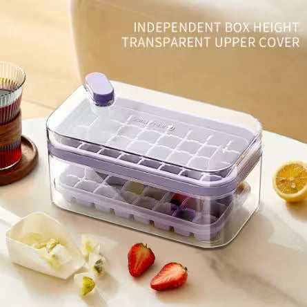 Ice cube tray with transparent top cover on a table with fruits and tea.