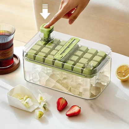 Green ice cube tray with clear lid on a kitchen counter, surrounded by fruits and a glass of juice.