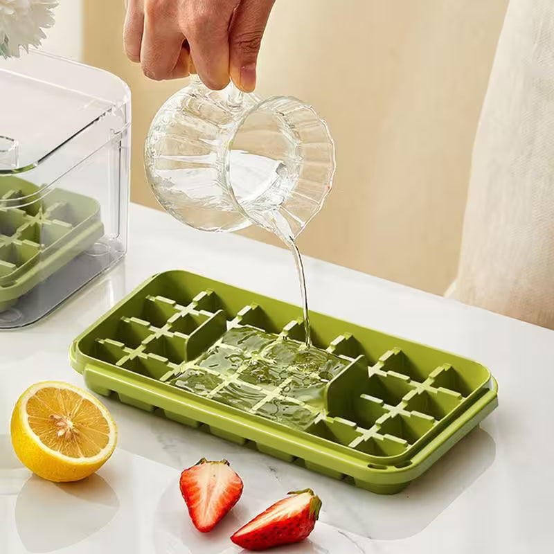 Person pouring liquid into a green silicone ice cube tray with fruits on a table.