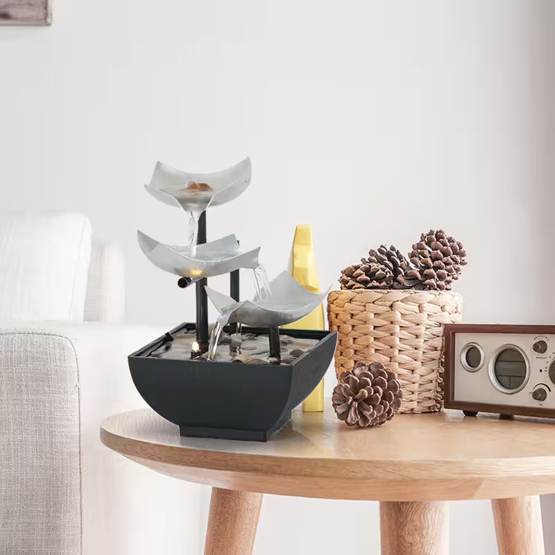 Decorative fountain on a wooden table with pinecones and a radio in a room setting.
