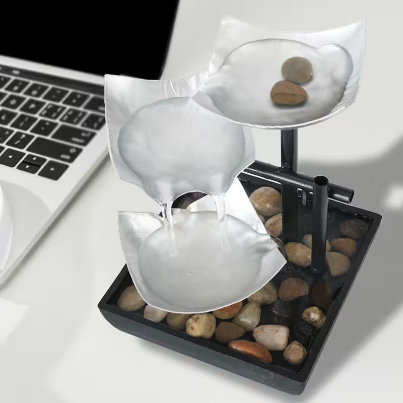 Small water fountain with stones on a desk next to a laptop