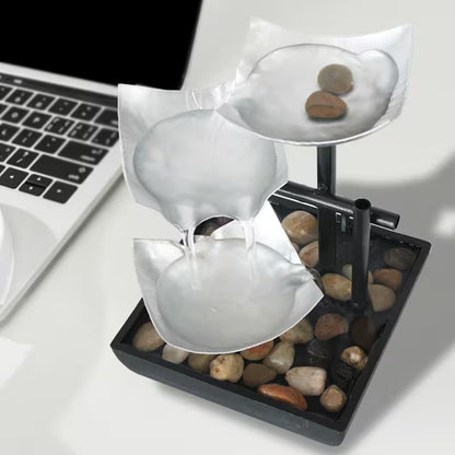 Small water fountain with stones on a desk next to a laptop