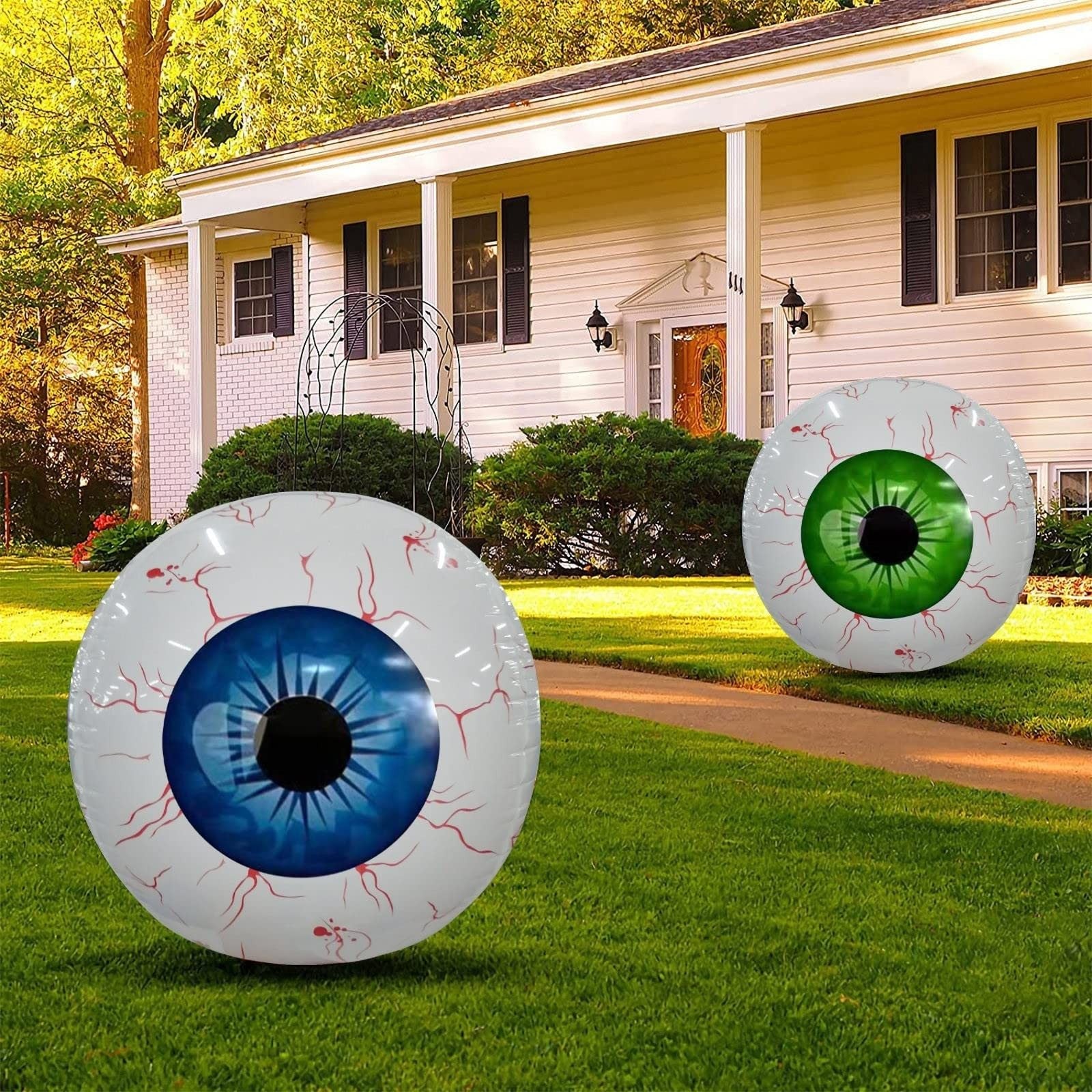 Two inflatable eye decorations on a grassy lawn in front of a house.