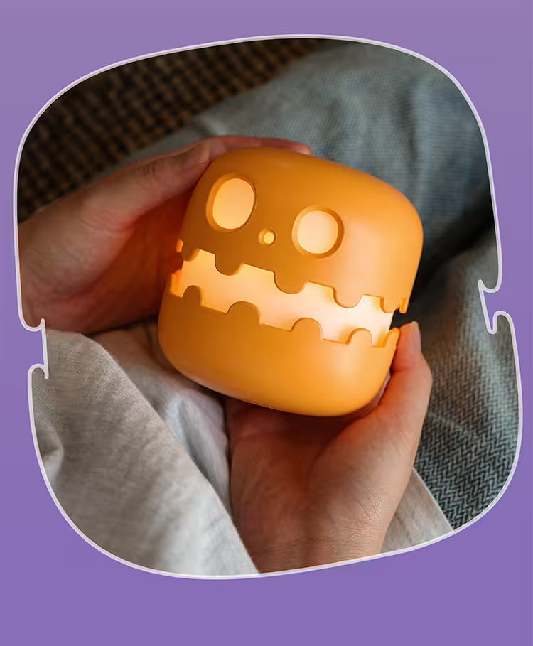 Hand holding a glowing orange pumpkin-shaped light with a purple border