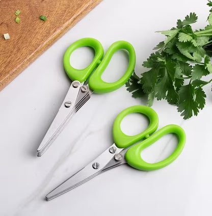 Two green-handled scissors on a white surface with fresh herbs.