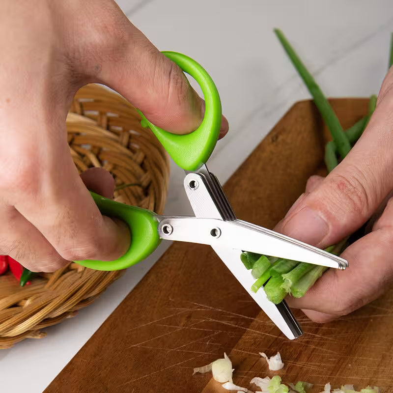 Person using green-handled scissors to trim green onions on a wooden cutting board.