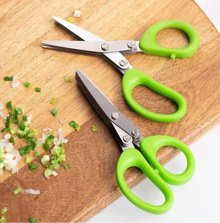 Green-handled scissors on a wooden cutting board with chopped vegetables.