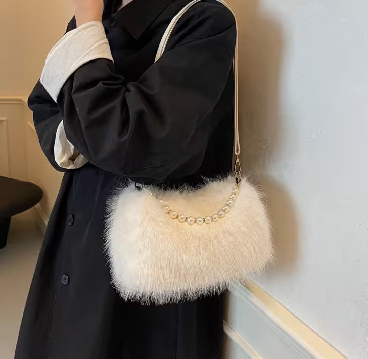 Person holding a fluffy handbag with pearl details against a neutral background