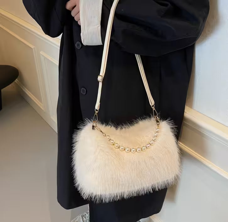 White fluffy handbag with pearl details held by a person wearing a black coat.