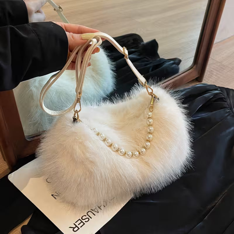 White fluffy handbag with pearl handle held by a person, placed on a black surface.