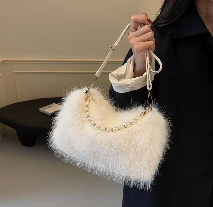 White fluffy handbag with pearl details held by a person indoors.