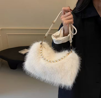 White fluffy handbag with pearl details held by a person indoors.