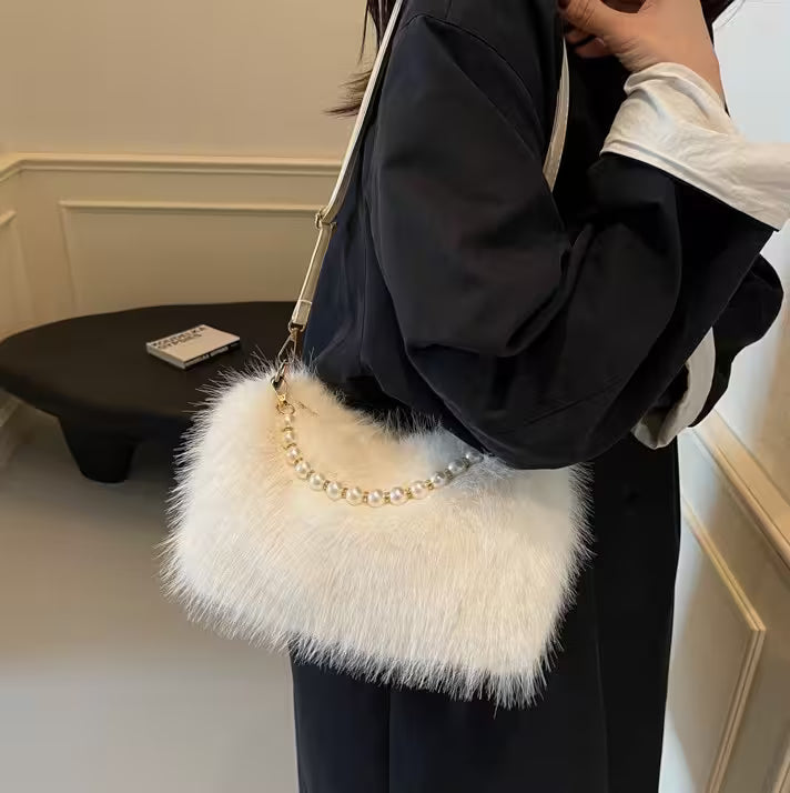 Person holding a white fluffy handbag with a pearl chain strap indoors.