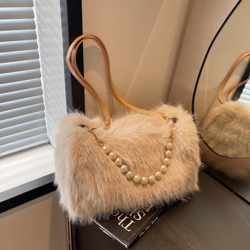 Fluffy beige handbag with a pearl necklace on a surface near a window.