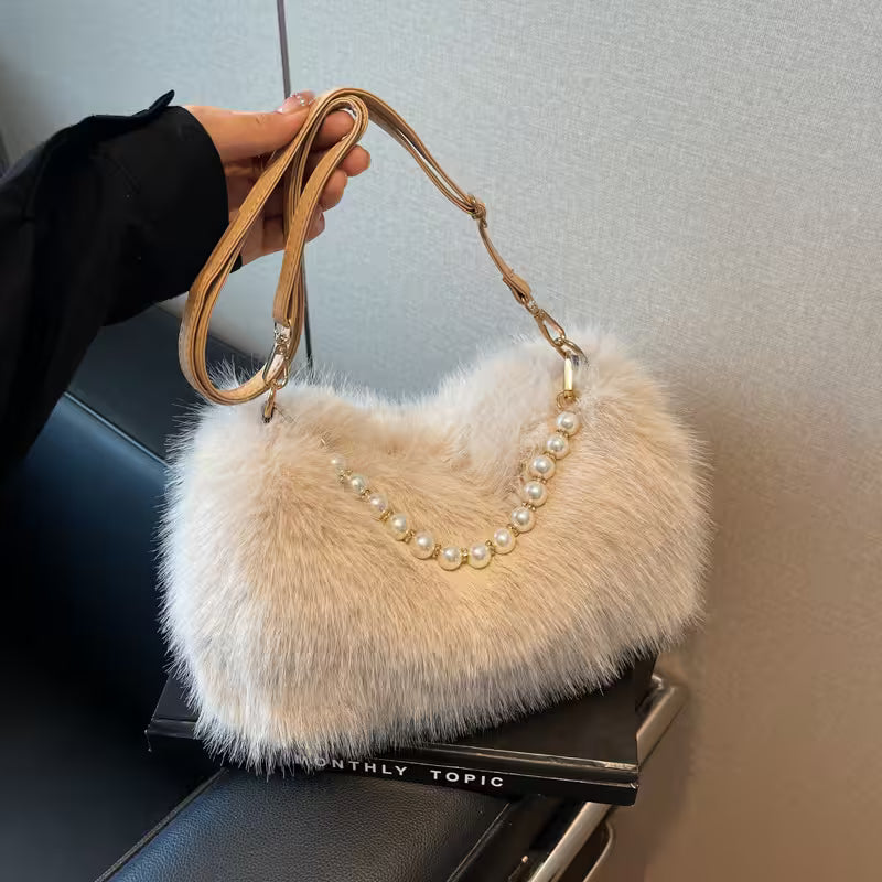 Beige fluffy handbag with pearl details held by a person against a neutral background