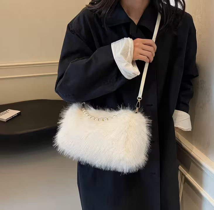 Person holding a white fluffy handbag with a chain detail indoors.