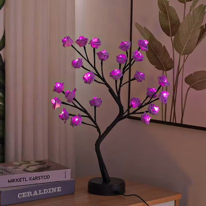 Decorative LED tree with purple flowers on a wooden surface next to books.