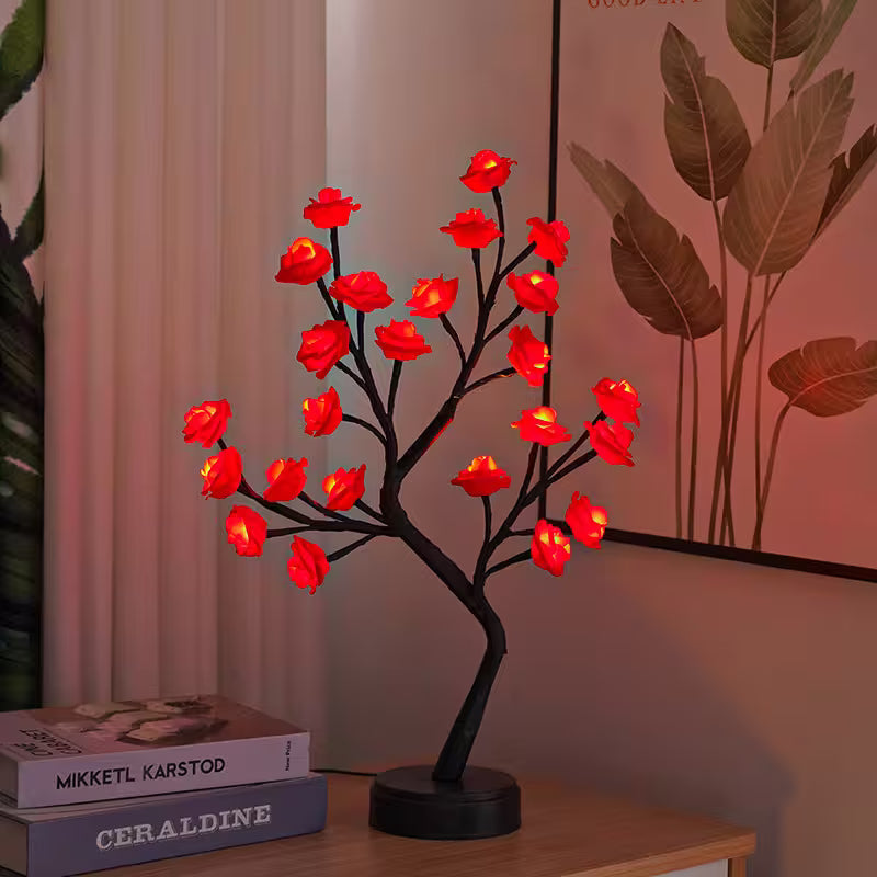 Decorative LED tree with red flowers on a wooden surface next to books.