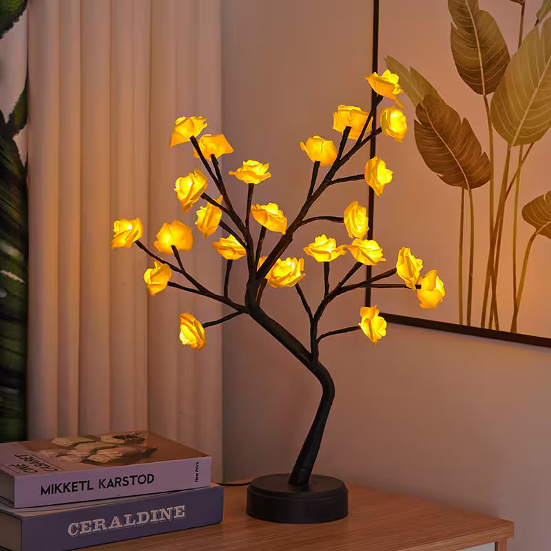 Decorative LED tree lamp with yellow lights on a table next to books