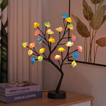 Decorative LED tree with colorful lights on a wooden surface next to books.