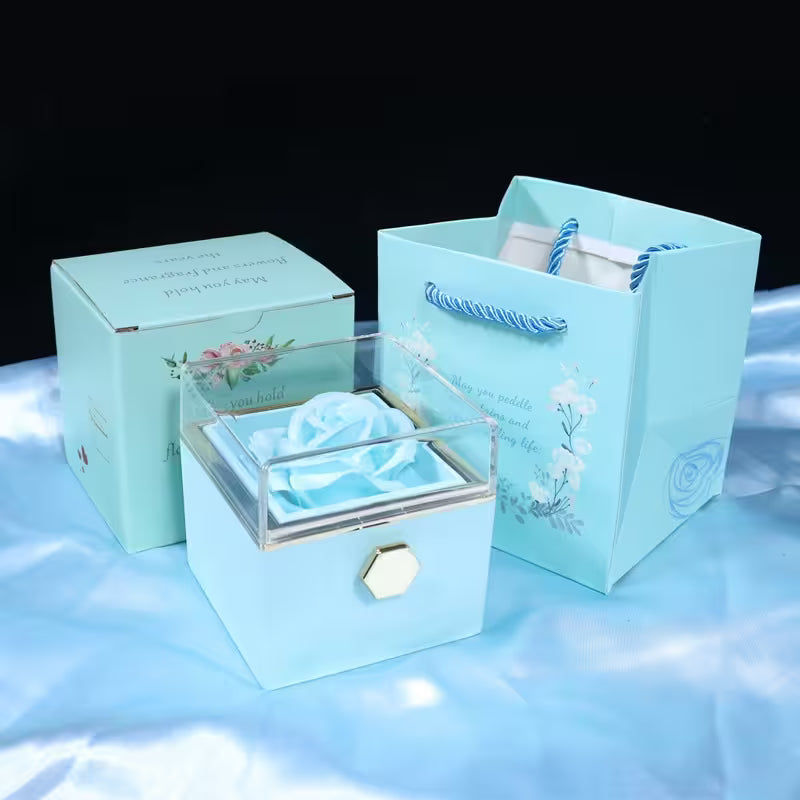 Set of light blue gift box, jewelry box, and bag with floral designs on a reflective surface.