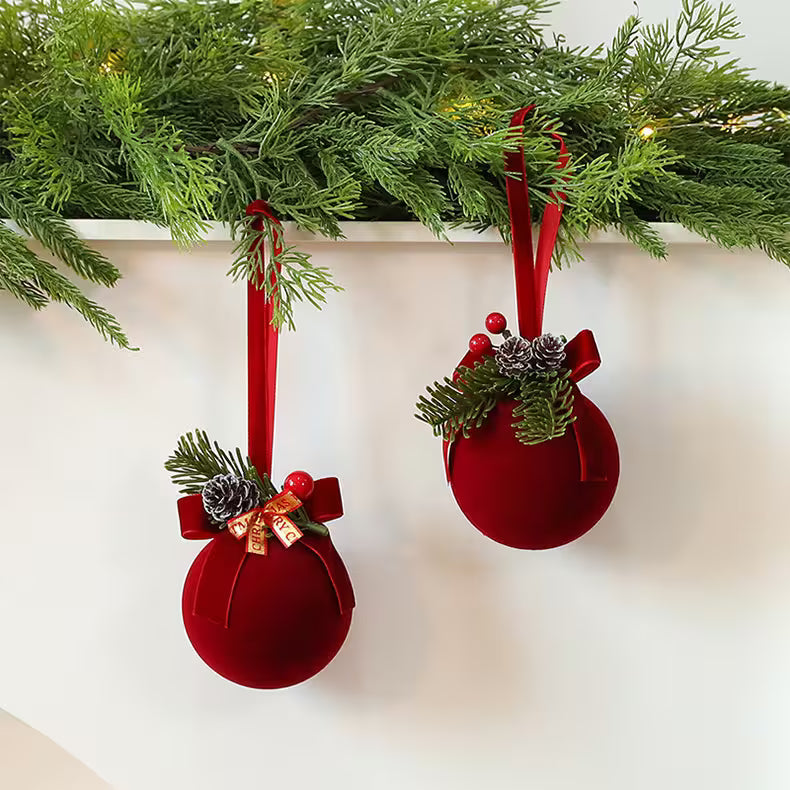 Two red Christmas ornaments with greenery and ribbons hanging against a white background.