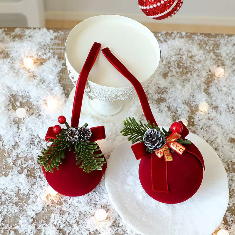 Red Christmas ornaments with greenery and ribbons on a snowy surface with lights.